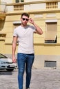 Portrait of handsome young man with sunglasses is posing and walking on urban city street. Male model photo-shoot outdoors. Royalty Free Stock Photo