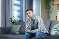 Portrait of a handsome young man. Waiting, bored, thought. Sits at home on the couch, holds his head in his hand, thinks Royalty Free Stock Photo