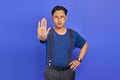 Portrait of handsome young man wearing blue shirt looking angry and doing stop gesture with palms on purple background Royalty Free Stock Photo