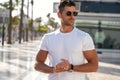 Portrait of handsome young man wearing sunglasses and white tshirt, posing on city street background. Casual style Royalty Free Stock Photo