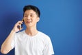 Portrait of a handsome young man in white t-shirt talking on mobile phone isolated over blue background Royalty Free Stock Photo