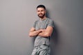 Portrait of a handsome young man who is standing leaning on a gray wall with his arms crossed, looking at the camera and smiling Royalty Free Stock Photo