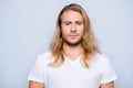 Portrait of handsome young serious confident young guy with blonde long hair in white tshirt, isolated on grey background Royalty Free Stock Photo