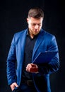 Portrait of handsome young successful man wearing dark shirt and blue suit holding blue folder Royalty Free Stock Photo