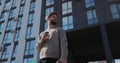 Portrait of hansome young caucasian man holding paper cup in hand at modern buildings in the background. Royalty Free Stock Photo