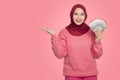 Portrait of the happiest Indonesian Muslim woman holding rupiah money isolated over pink background and copy space