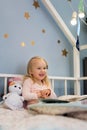 Portrait of happy adorable girl reading book while sitting in bed with lights Royalty Free Stock Photo