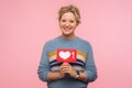 Portrait of happy adult woman with curly hair in warm sweater holding heart Like icon, love content Royalty Free Stock Photo