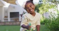 Portrait of happy african amercian girl watering plants holding spray bottle in garden