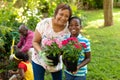 Portrait of happy african american boy and grandmother carrying potted flowering plants in backyard