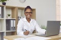 Portrait of happy African American businesswoman at office desk with paperwork and laptop Royalty Free Stock Photo