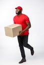 Portrait of Happy African American delivery man in red cloth walking to send a box package to customer. Isolated on Grey Royalty Free Stock Photo