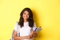 Portrait of happy african-american female college student, holding notebooks and backpack, smiling and standing over Royalty Free Stock Photo