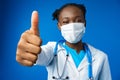 Portrait happy African American female doctor showing ok sign in blue studio Royalty Free Stock Photo