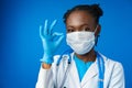 Portrait happy African American female doctor showing ok sign in blue studio Royalty Free Stock Photo