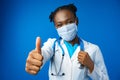Portrait happy African American female doctor showing ok sign in blue studio Royalty Free Stock Photo