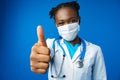 Portrait happy African American female doctor showing ok sign in blue studio Royalty Free Stock Photo