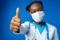 Portrait happy African American female doctor showing ok sign in blue studio Royalty Free Stock Photo