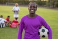 Portrait of happy african american goalkeeper with soccer ball standing in playground at sunset Royalty Free Stock Photo