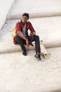 Happy african american guy sitting outside on steps with mobile phone and skateboard Royalty Free Stock Photo
