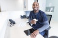 Portrait of happy african american male doctor holding tablet and takeaway coffe at reception desk Royalty Free Stock Photo