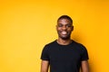 Portrait of a happy African American man in a black t-shirt smiling at the camera. Isolated on yellow background Royalty Free Stock Photo