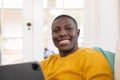 Portrait of happy african american man on couch at home using tablet smiling to camera Royalty Free Stock Photo