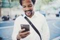Portrait of Happy African American man in headphone walking at sunny city and enjoying to music on his smartphone Royalty Free Stock Photo
