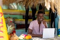 Portrait of happy african american man using laptop behind counter of surf hire beach shack Royalty Free Stock Photo