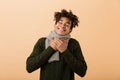 Portrait of happy african american man wearing sweater and scarf touching throat, isolated over beige background Royalty Free Stock Photo