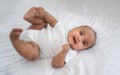 Portrait of happy African American mixed race cute girl baby lying down on white bed and look on camera in a bedroom at home Royalty Free Stock Photo