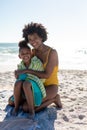 Portrait of happy african american mother and daughter sitting on sand at beach during sunny day Royalty Free Stock Photo