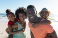 Portrait of happy african american parents giving piggyback rides to children at beach on sunny day Royalty Free Stock Photo