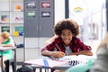 Portrait of happy african american schoolboy writing at desk, with diverse pupils, copy space