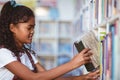 Portrait of happy african american schoolgirl taking book from shelf in school library