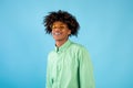 Portrait of happy african american teen guy in mint shirt and yellow sunglasses posing on blue studio background Royalty Free Stock Photo