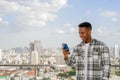 Portrait of happy African black man outdoors in city at rooftop during summer using mobile phone while smiling Royalty Free Stock Photo