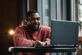 Portrait of happy african businessman using phone while working on laptop in restaurant. Royalty Free Stock Photo