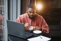 Portrait of happy african businessman using phone while working on laptop in restaurant. Royalty Free Stock Photo