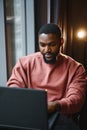 Portrait of happy african businessman using phone while working on laptop in restaurant. Royalty Free Stock Photo