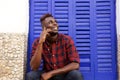 Happy african man sitting outdoors talking on mobile phone and looking away Royalty Free Stock Photo