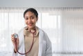 Portrait of happy African woman professional doctor in uniform standing holding stethoscope and look at camera in white room at Royalty Free Stock Photo