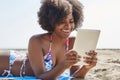 Happy afro american woman lying on beach reading ebook Royalty Free Stock Photo