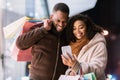 Portrait of happy afro couple using smartphone with shopping bags Royalty Free Stock Photo