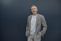 Portrait of happy aged gray haired businessman enjoying and standing with hands in pants pockets in stylish suit on gray Royalty Free Stock Photo