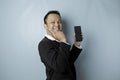 A portrait of a happy Asian businessman is smiling and holding his smartphone pointing copy space beside him wearing black suit Royalty Free Stock Photo