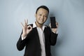 A portrait of a happy Asian businessman is smiling and holding his smartphone showing copy space on it`s screen and gesturing Ok Royalty Free Stock Photo