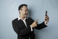 A portrait of a happy Asian businessman is smiling and holding his smartphone wearing black suit isolated by a blue background Royalty Free Stock Photo