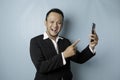 A portrait of a happy Asian businessman is smiling and holding his smartphone wearing black suit isolated by a blue background Royalty Free Stock Photo