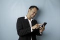 A portrait of a happy Asian businessman is smiling and holding his smartphone wearing black suit isolated by a blue background Royalty Free Stock Photo